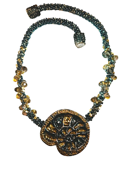 24 karat gold accents on a fine silver rehouse of an ammonite with a handmade 8 strand Kumihimo necklace of glass beads and faceted crystal beads with a laminated 24 gold interiors.